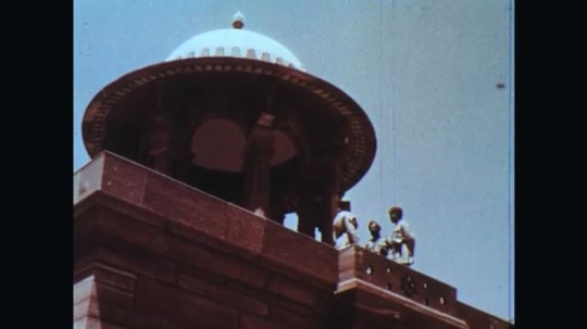 INDIA: 1960s: Men talk on roof of building. People walk up steps of building. Lady carries basket on her head. 