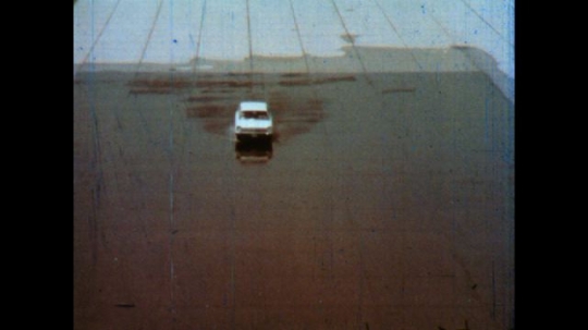 United States: 1980s: car travels across wet surface and slides. Car drives through obstacle course on wet road. Car knocks over cones. Cars slides on wet surface
