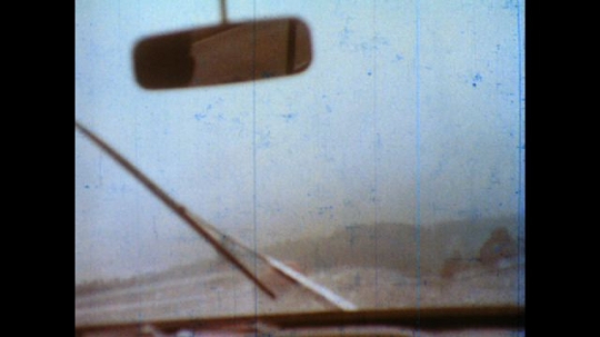 United States: 1980s: view through wipers on car windscreen. Cars and lorries drive up hill in rain. 