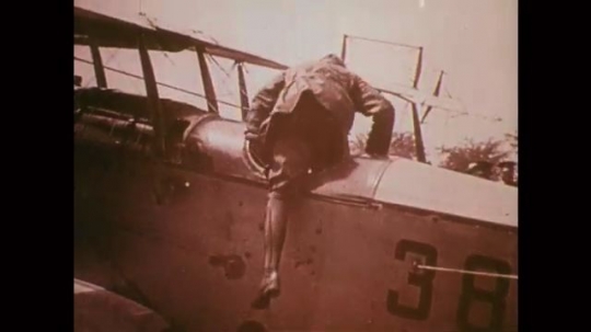 1918: Pilot climbs to cockpit of plane. President Wilson stands in crowd, crosses arms. Pilot in cockpit. Airplane takes off, army men watch. Airplane takes off. Aerial landscape, buildings. 