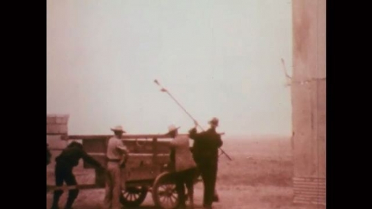 1920s: Men lift pole, box from cart. Men, wood stilts. Men watch from outpost. Rocket launches, explodes in sky. Man with headset turns control panel switch. Man records radio. Truck drives by plane. 