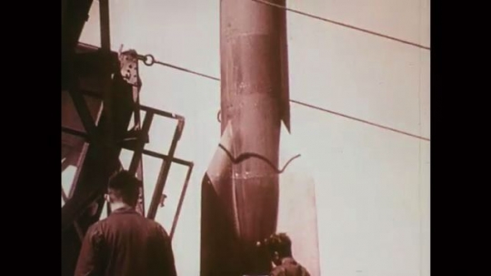 1930s: Two men with standing missile. Weather vane. Missile launches from shore to sky, explodes, parachute deploys, missile falls. 