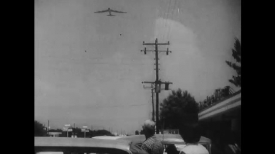 UNITED STATES: 1960s: plane in sky. People look up at plane. Lady points in air. Man catches bomb