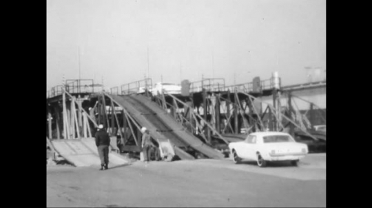 UNITED STATES: 1960s: cars drive up ramp towards men. 