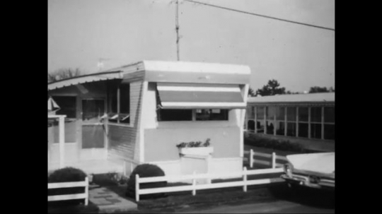 UNITED STATES: 1960s: caravans and trailers at park. Umbrella and table outside trailer