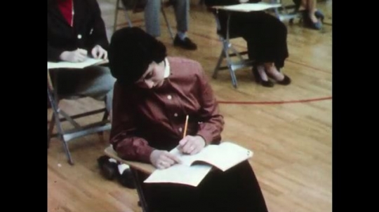 UNITED STATES: 1950s: girl takes exam. Students in exam hall. Lady listens to girl