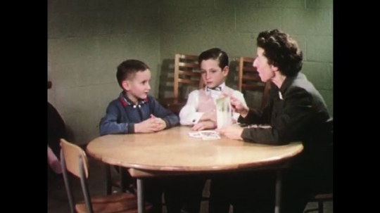 UNITED STATES: 1950s: lady talks to children at desk. Trainees make notes during observation