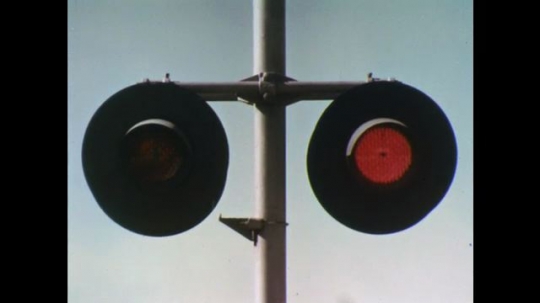 UNITED STATES: 1970s: railway crossing lights. Train travels over road. Stop on red signal sign. 