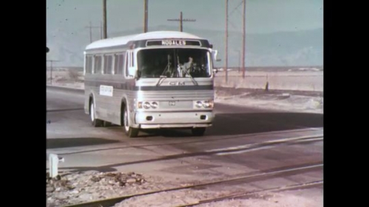 UNITED STATES: 1970s: bus waits at railway crossing. Railway signal lights. View from train