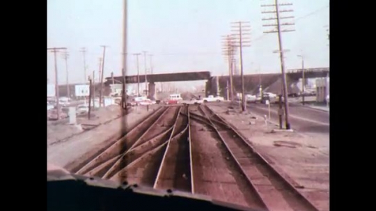 UNITED STATES: 1970s: view from train as it approaches crossing. Cars on crossing. Man by tracks.