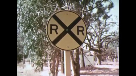 UNITED STATES: 1970s: railway crossing sign. View through car window. Railway crossing signal. Train approaches crossing