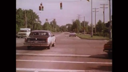UNITED STATES: 1980s: cars drive along road. Parked car hazard. Car drives behind slow truck