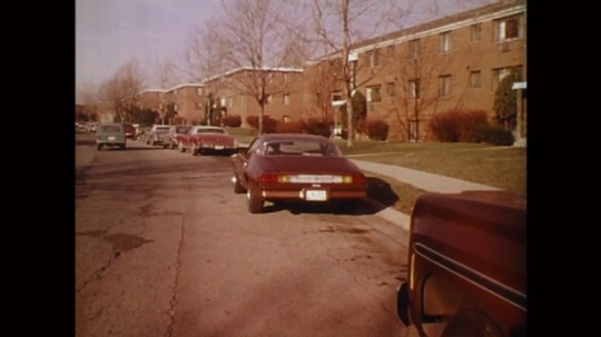 UNITED STATES: 1980s: cars parked outside buildings on street. Arrow points to driver of parked car. Arrow points to indicator on car. 