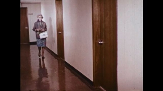 UNITED STATES: 1960s: lady walks along corridor to apartment. Door open. Lady finds stranger in her apartment