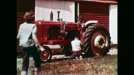1950s: Boy working on tractor, girl approaches. Boy talks to girl in foreground. Close up, girl talking. Girl walks away. Pan of young people in audience. 