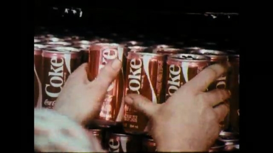 1970s: Hands arrange soda cans in display. Man making display, zoom out. Hand held shot, entering store. Man drives truck, talks. 