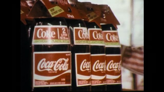 1970s: Bottles of soda, man cleans shelf. Man wiping behind shelf. 
