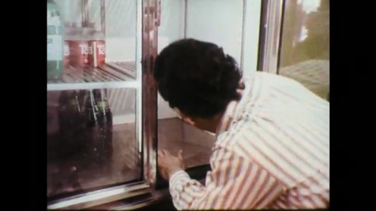 1970s: Man cleans display case. Man closes door to case, talks into camera. High angle view of downtown Chicago. 