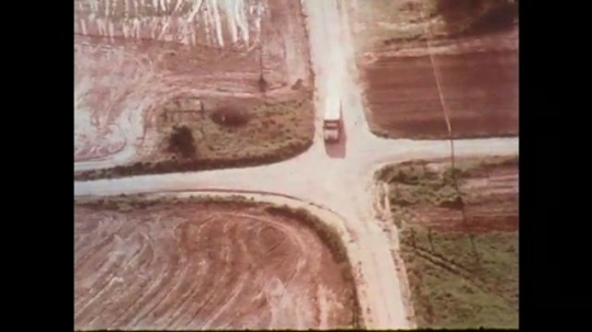 1970s: Aerial view of truck driving on road. Truck in front of store, man unloads pallets. 