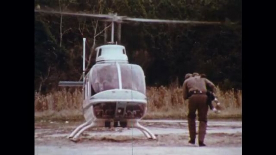 UNITED STATES: 1970s: officer carries lost boy to helicopter in woods. 