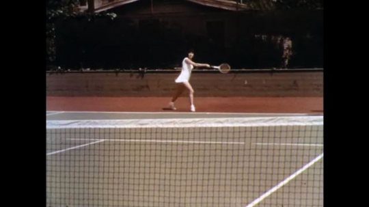 UNITED STATES: 1960s: lady plays tennis. German Shepherd dog watches lady play tennis. Ladies shake hands in tennis court.