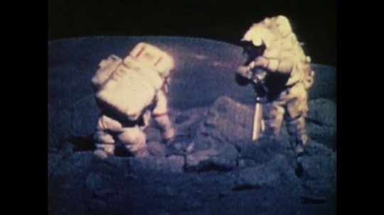 1970s: UNITED STATES: astronauts collect rocks on moon. Astronaut bounces across moon surface. Surface rocks on planet.