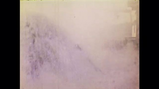 1970s: UNITED STATES: water sprays on deck of oil rig. Divers jump into sea from oil rig. Diver works underwater. Men on oil rig. Waves around oil rig platform