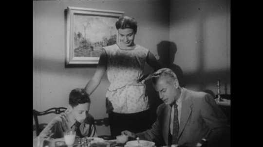 1950s: UNITED STATES: man and boy eat meal. Lady talks with family at table. Girl talks to lady
