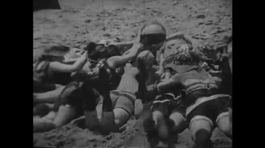1920s: women in swimsuits dogpile and fight for ball on beach sand. women exit igloos and throw snowballs. women pelt man in fur with balls. 