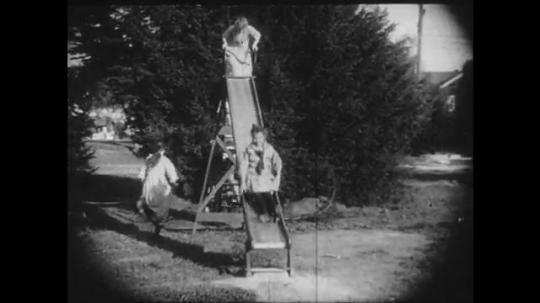 1910s: Girls play on a slide, another girl attempts to joint the fun but the group rejects her. A girl on a bench gets up and leaves her dolls behind.