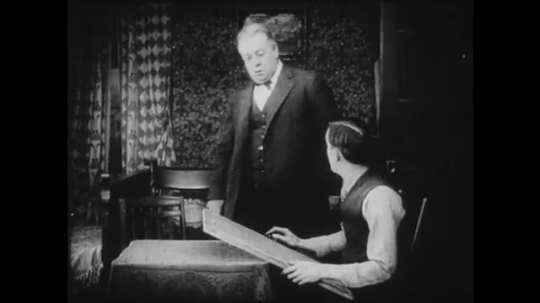 1910s: Older man walks into room that younger man is in. Younger man shows a drawing of the older man he has made. They have a conversation. Young girl crouches and talks to adult woman.