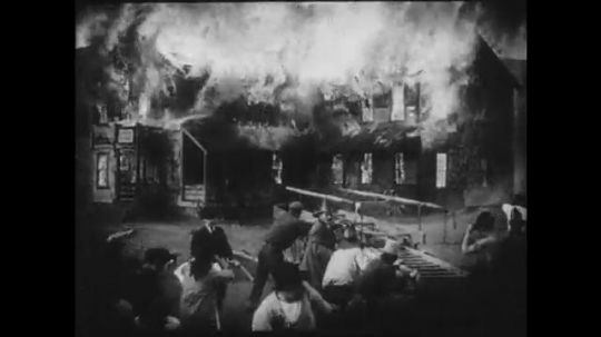 1910s: A building burns while firefighters flee from the scene. An elderly woman tucks a young girl into bed.