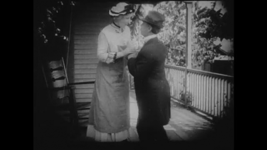 1910s: Man and woman greet each other on a porch. Young girl throws rocks at a boy to get his attention. Shows him her new hair style and outfit.