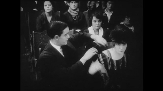 1910s: Young couple watch a movie in a theater, the girl removes her jacket. The movie is a Western.