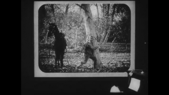 1910s: First-person-point-of-view in a movie theater. Movie is a Western of an outlaw being captured.