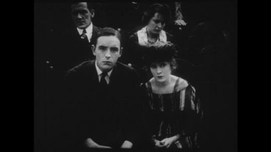 1910s: Young couple watches a movie in a theater, they start to hold hands nervously.