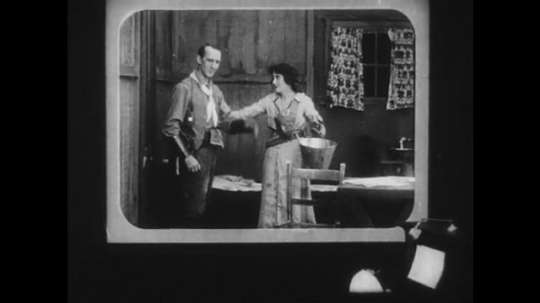 1910s: First-person-point-of-view in a movie theater. Movie shows a woman hugging a man, going outside, then someone shooting the man from outside.