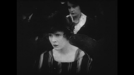 1910s: Young couple watches a movie in a theater, they watch the screen with apprehension. Movie shows woman realizing that her lover has been shot.
