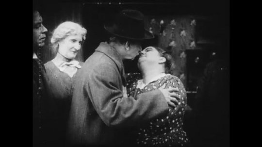 1910s: Couple kisses. Someone brings the woman a cat, saying it has been shot - it is still alive, though. Young woman giggles to a young man next to her.