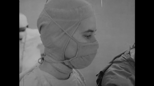 1950s: Medical professionals in scrubs and masks look down. Hand uses instrument on brain. Medical professional sits next to patient.