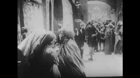 1910s: UNITED STATES: women carry water through village street. Ladies greet each other in street. Lady carries baby. 