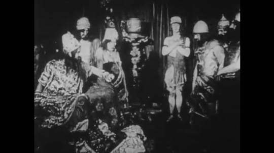 1910s: UNITED STATES: men stand around leader on throne. Lady walks to window. 