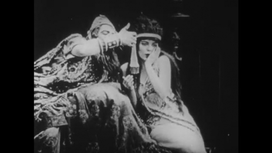 1910s: UNITED STATES: man on throne drinks from goblet. Lady comforts man. Man collapses in lady