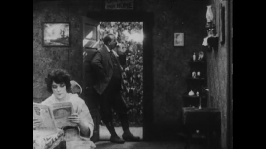 1910s:  man smokes cigarette in doorway, puts on cowboy hat, escorts woman to door, hugs and exits. man mounts and rides horse in woods.  woman waves and blows kiss.