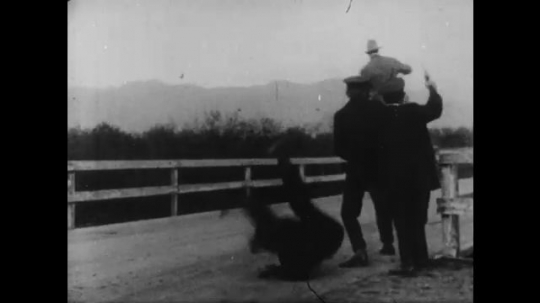 1910s: man in cowboy hat on a horse fires gun and chases man with mustache on motorcycle with woman in sidecar. Three men in police uniforms shoot, look in telescope, run and board rowboat on water.
