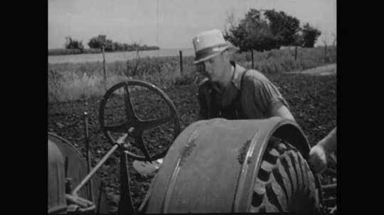 1930s: Boy climbs on tractor, pushes lever. Boy starts tractor, plows field. 