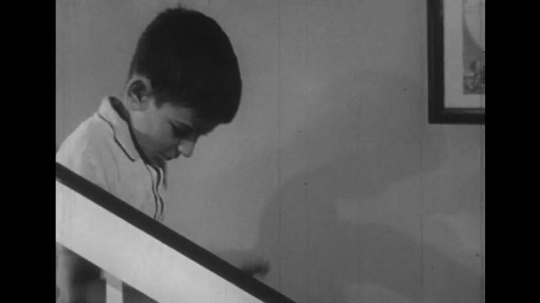 1950s: Boy walks down stairs. Pan to stairs, man talks to boy. Close up of boy. 