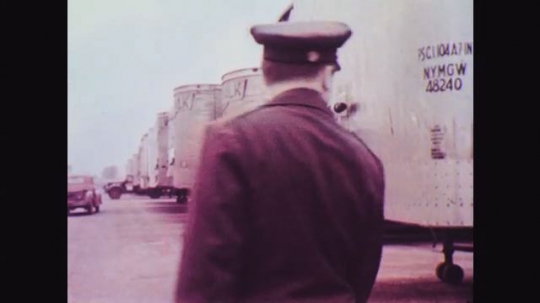 1950s: Man in uniform looks at parked trailers. Truck marked Norwalk Truck Lines drives through parked tractor trailers in yard. Man in uniform walks behind Norwalk truck.