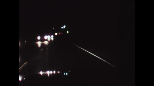 1970s: UNITED STATES: view through car windscreen at night. Incoming car on road. 