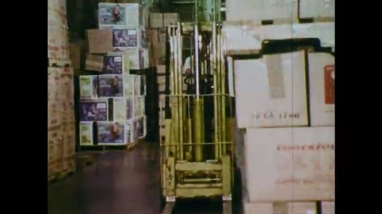 1970s: UNITED STATES: man drives truck in warehouse. Man lifts load with truck. 